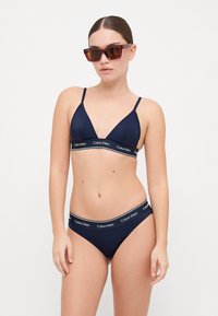 Hellblaues Bikiniset mit einem dreieckigen Bralette und verstellbaren Trägern sowie passenden tief sitzenden Unterteilen, beide mit weißen Logo-Bandelementen.