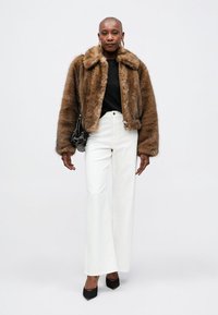 Brun faux fur jacka med krage, svart zip-up topp under, vita vida byxor och svarta högklackade skor. Svart väska med detaljer.