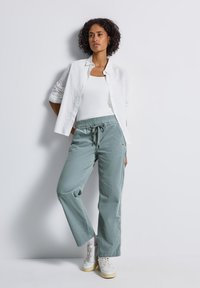 Pantalons légers verts, amples, avec une taille élastique et un cordon de serrage, associés à une chemise blanche à boutons et des baskets.