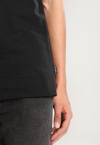 Svart bomullströja med rak passform, korta ärmar och en sydd etikett på sidan. Tillsammans med mörkgrå byxor.