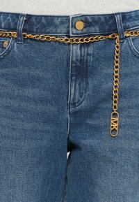 Blue denim jeans feature a gold chain belt and a decorative safety pin accent, detailed with classic five-pocket styling and a zip fly.