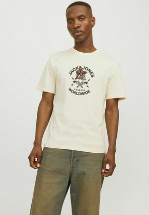 Krém színű pamut póló, középen egy kalapos koponyát ábrázoló grafikával, körülötte a "JACK&JONES WORLDWIDE" felirattal és villámcsapásokkal.