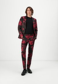 Anzug mit schwarzem Hintergrund und rotem Blumenmuster; umfasst ein schwarzes Hemd, eine schlanke Jacke und Hosen. Die Schuhe sind schwarze Loafers.