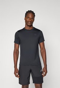 Μαύρο αθλητικό μπλουζάκι με κοντά μανίκια, απαλό ύφασμα, στρογγυλή λαιμόκοψη, διακριτό λογότυπο στο στήθος, συνδυασμένο με μαύρες βερμούδες που έχουν πλαϊνή τσέπη.