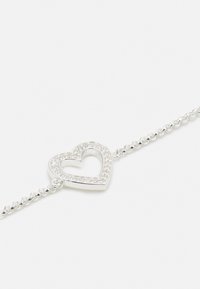 Pulseira de prata com um encantador pingente em forma de coração com um centro recortado, decorado com pequenos detalhes metálicos ao longo da borda. Design de elos de corrente.