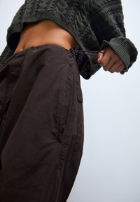 Bruine cargo shorts met een verstelbare tailleband, zichtbare zakdetails en een losse pasvorm, gecombineerd met een gestructureerde donkergroene gebreide trui.