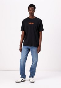 Tricou negru din bumbac cu guler rotund, având textul portocaliu "Creative Works". Asortat cu blugi ușor albaștri și adidași alb-negru.