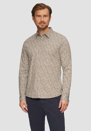 Beige overhemd met lange mouwen en een subtiel stippenpatroon, met een button-down kraag en een zachte textuur. Draagt met marineblauwe broek voor contrast.