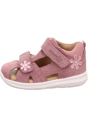 Różowe zamszowe sandały z wycięciami i regulowanym paskiem. Ozdobione różowymi kwiatami z metallicznym srebrnym środkiem. Biała gumowa podeszwa.