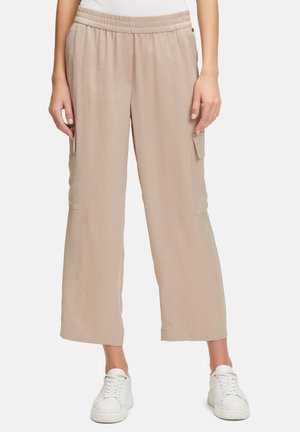 Beige, wide-leg cargo pants with elastic waistband. Features two side pockets and a smooth, lightweight fabric, paired with white sneakers.