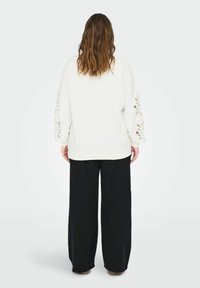 Felpa crema con ritagli floreali sulle maniche, abbinata a pantaloni neri a gamba larga, completata da un fit rilassato e un design casual.