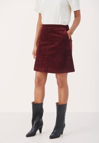 Falda de pana burdeos en corte A con bolsillos laterales, combinada con botas de cuero negras de tacón hasta la rodilla. Top sencillo blanco de manga corta.
