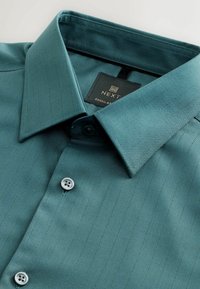 Teal dress shirt with a pointed collar, featuring vertical pinstripes, button closures, and a branded label on the neckline.