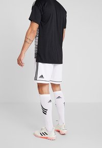 Jersey negra de manga corta con la parte trasera a rayas, pantalones cortos blancos, calcetas blancas hasta la rodilla con tres rayas negras y botas de fútbol en blanco y negro.