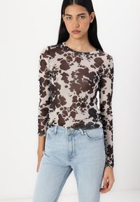 Långärmad topp i genomskinligt brunt och grått ko-mönster, rund halsringning, tillsammans med ljus tvättade högmidjade jeans.