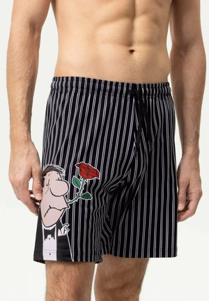 Pantaloncini a righe verticali bianco e nero con un uomo dei cartoni animati in smoking che tiene una rosa rossa sulla coscia sinistra, indossati da una persona senza maglietta.