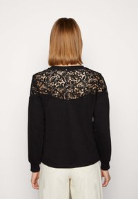 Maglione nero con un pannello posteriore in pizzo con motivi floreali, maniche lunghe e scollatura rotonda, realizzato in tessuto morbido.