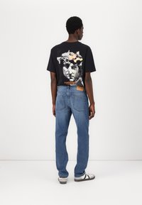 Tricou grafic negru cu un design împărțit al unei busturi clasice. Blugi din denim albastru deschis cu o croială dreaptă și pata de piele pe spate. Încălțăminte casual.