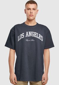Tumši pelēks pārspīlēts T-krekls ar tekstu "LOS ANGELES" baltā krāsā krūtīs un smalku izliekumu. Brīva piegriezuma, īsas piedurknes.