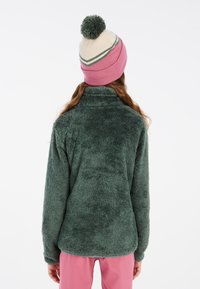 Giacca in pile verde con colletto alto, morbida al tatto e maniche lunghe. Accompagnata da un berretto a righe rosa e crema con un pompon sulla cima.