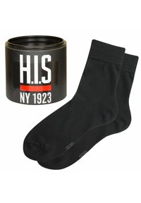 Svarta bomullssockor visade bredvid en rund svart behållare märkt "H.I.S NY 1923" i vit och röd text, slät textur, enkel design.