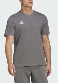 Graues V-Ausschnitt-T-Shirt aus Baumwolle, mit einem weißen Adidas-Logo auf der linken Brust und kurzen Ärmeln. Glatte Textur, lässige Passform.