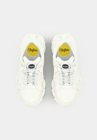 White sneakers with a chunky sole and textured leather upper. Features gray laces, a black logo on the tongue, and a bright yellow insole.