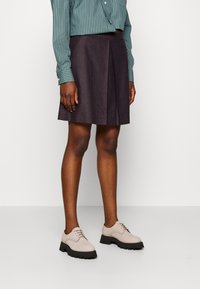 Gonna a pieghe a scacchi scuri abbinata a una camicia button-up a righe verde e scarpe lace-up rosa chiaro con suole nere.
