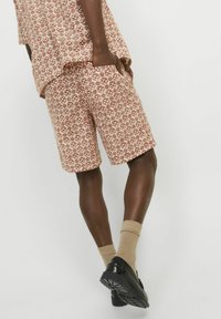 Shorts en coton à motifs dans des tons rouge-brun, présentant un design géométrique, des poches latérales et une coupe décontractée, associés à des chaussettes et des chaussures beiges.