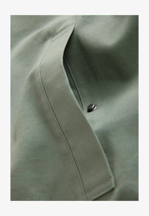 Grön tyg med en mjuk textur har en sidficka och en silverfärgad tryckknapp, vilket visar en vikt design.