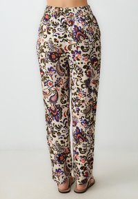 Pantalons à motifs beige avec des dessins floraux et paisley en violet, rouge et vert. Dotés d'une taille élastique et d'une coupe ample.