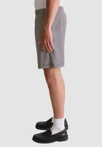 Geruite shorts in zwart en wit, met een ontspannen pasvorm, lichte stof en zijzakken, gedragen met zwarte loafers en witte sokken.