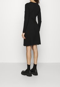 Robe noire à manches longues avec un ourlet évasé, en tissu tricoté. Complétée par des chaussures noires à semelle épaisse et des chaussettes assorties.