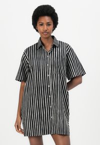 Čierno-biely pruhovaný krátky rukáv košeľa, s gombíkmi na prednej strane, klasický golier, jedna náprsné vrecko, voľný strih. Hladká textúra látky.