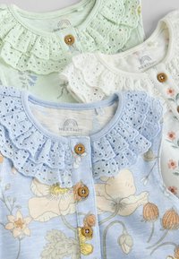 Three baby cardigans in pale green, white, and blue, featuring a ruffled collar, floral patterns, and wooden button closures.