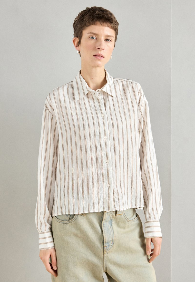 Garu piedurņu pogājama krekls gaiši bežā krāsā ar plānām vertikālām svītrām. Iespējama klasiskā apkakle un kontrastējoši svītroti piedurkņu gali. Tekstūrēta auduma.