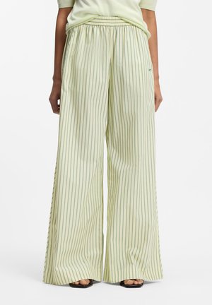 Široke kremne hlače z ozkimi zelenimi navpičnimi črtami, oblečene z svetlo zelenim topom in črnimi sandali z odprtimi prsti.