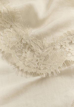 Tissu de couleur crème avec une délicate bordure en dentelle florale comportant un fin filet et des bords festonnés, disposé en plis souples.