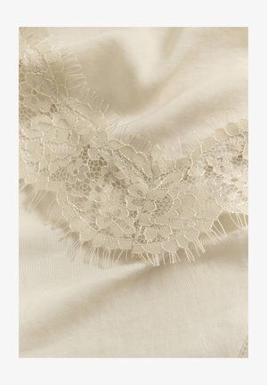 Tissu de couleur crème avec une délicate bordure en dentelle florale comportant un fin filet et des bords festonnés, disposé en plis souples.