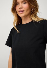 Zwart katoenen T-shirt met korte mouwen en een ronde hals. Gladde textuur, cropped ontwerp, minimale details.