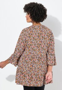 Tunic con stampa floreale su sfondo scuro, dotata di maniche a campana a tre quarti, vita arricciata e vestibilità comoda. I colori includono rosa, arancione e bianco.