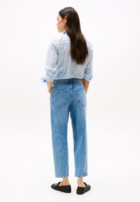 Jeans de denim azul de cintura alta con corte recto, que cuentan con dos bolsillos traseros y una textura desgastada. Combinados con una camisa azul clara.