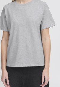 Pilkas medvilnės marškinėliai trumpomis rankovėmis su apvalia iškirpte. Lygus audinys ir laisvas siluetas, derinami su juoda sijonu, kurio liemuo aiškiai matomas.