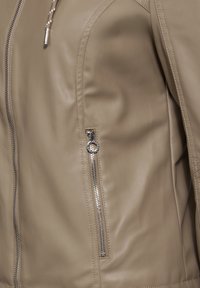 Giacca in pelle beige con una texture liscia, dotata di una tasca con zip laterale e dettagli in hardware argentato, enfatizzando un design minimalista.