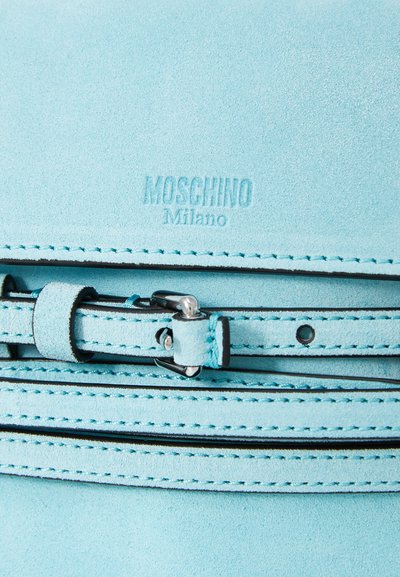 Világoskék velúr táska fekete varrással, ezüst csattal és dombornyomott "Moschino Milano" logóval. Simaság jellemzi, jól strukturált dizájnnal.