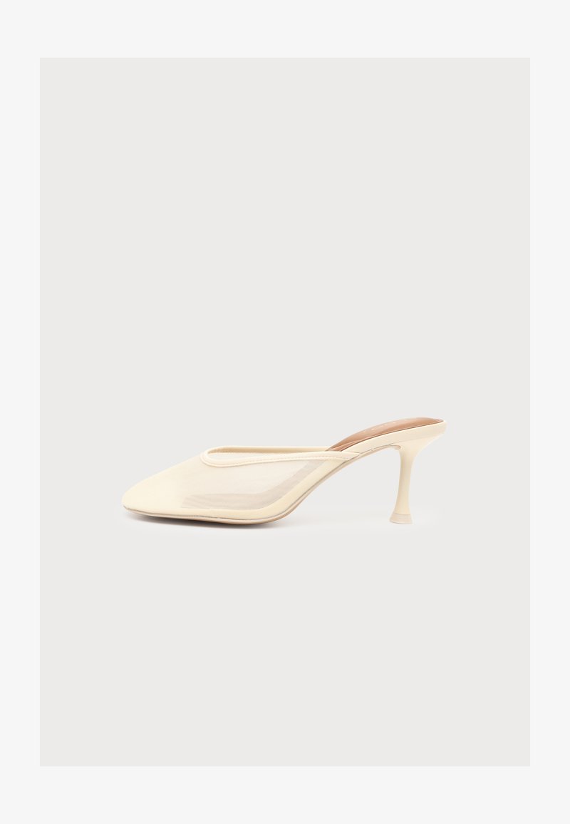 Mule en maille beige à bout pointu et talon évasé de hauteur moyenne, présentée de profil sur fond clair et uni.