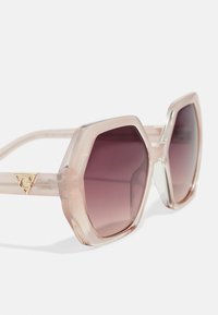 Hexagonal sunglasses with a light pink transparent frame and gradient dark lenses. Features a gold logo accent on the temple.