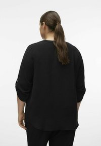 Svart, texturerad topp med trekvartslånga ärmar, rund halsringning och subtila sidöppningar. Bakifrån visar den en avslappnad passform och slät finish.