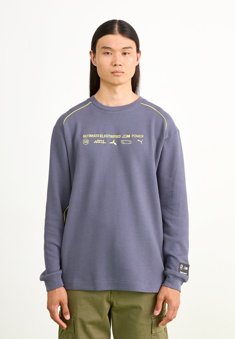 Lilla langærmet sweatshirt med tekstureret stof, gule detaljer og trykte logoer. Har en ribbet hals og manchetter.