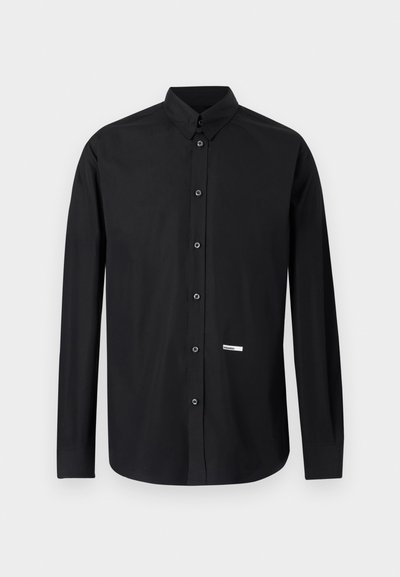 Sort langærmet skjorte med knapper, spidst krave og lille hvidt rektangulært mærke nær nederste højre front.